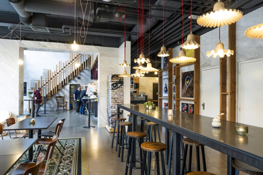 Modern interior of a café at Laan van Kronenburg with industrial design, hanging lights, and artwork on the walls.
